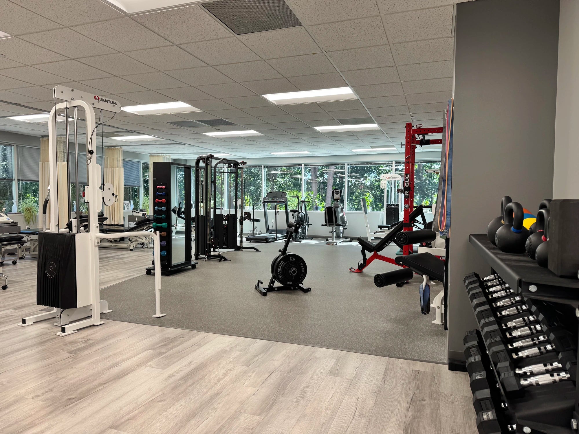 Gym interior with various exercise equipment and large windows.